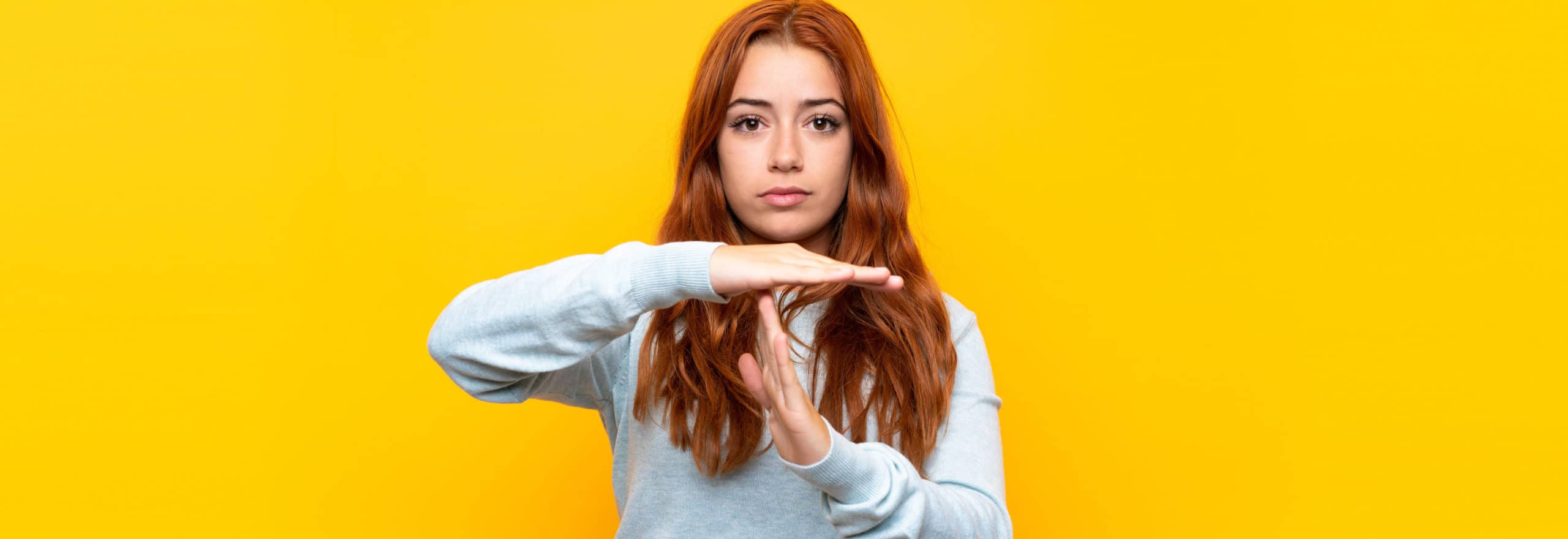 Teenager redhead girl over isolated yellow background making time out gesture Von luismolinero